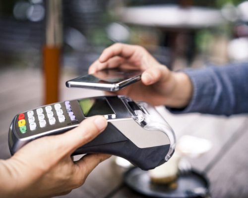 Close-up of customer paying for his coffee through mobile payment. Owner is holding credit card reader. They are in cafe.