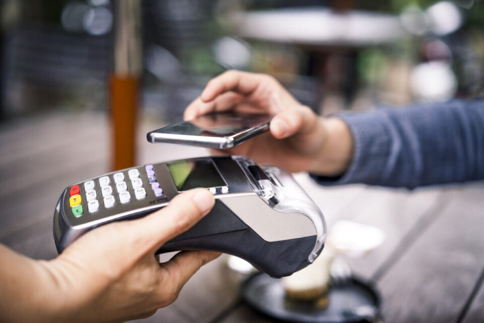 Customer paying using mobile payment to cafe owner Close-up of customer paying for his coffee through mobile payment. Owner is holding credit card reader. They are in cafe.